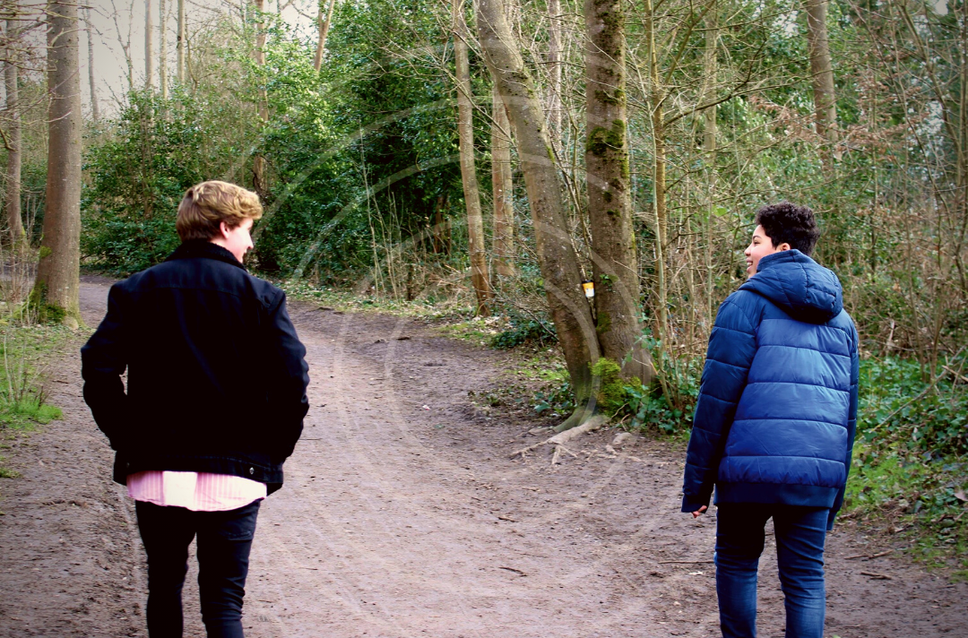 Photo shows two young people walking along a wooded path with their backs to the camera. White circles have been overlaid to look like they are resonating out of the young people..