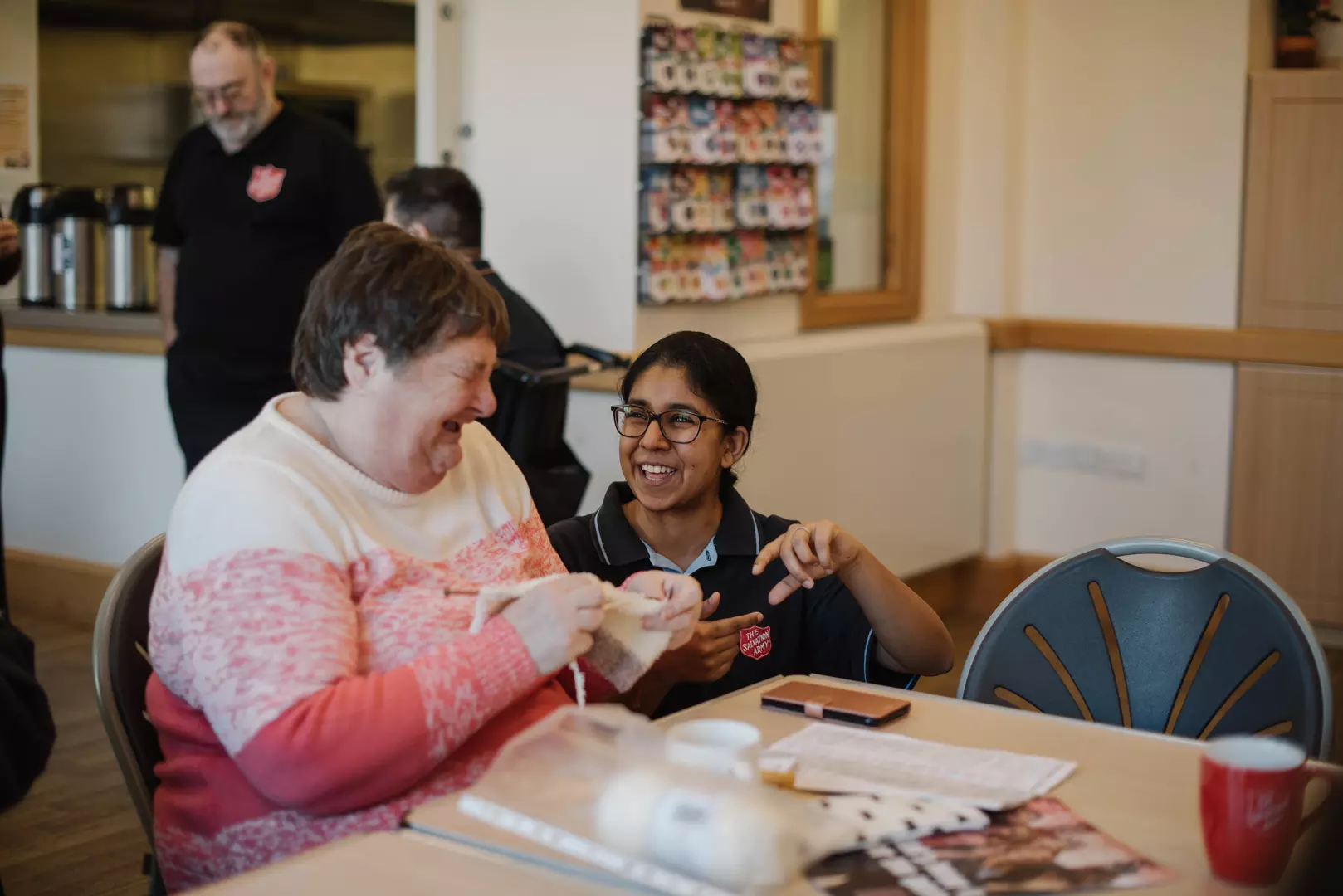 Photo shows two people smiling and laughing while sat at a table.