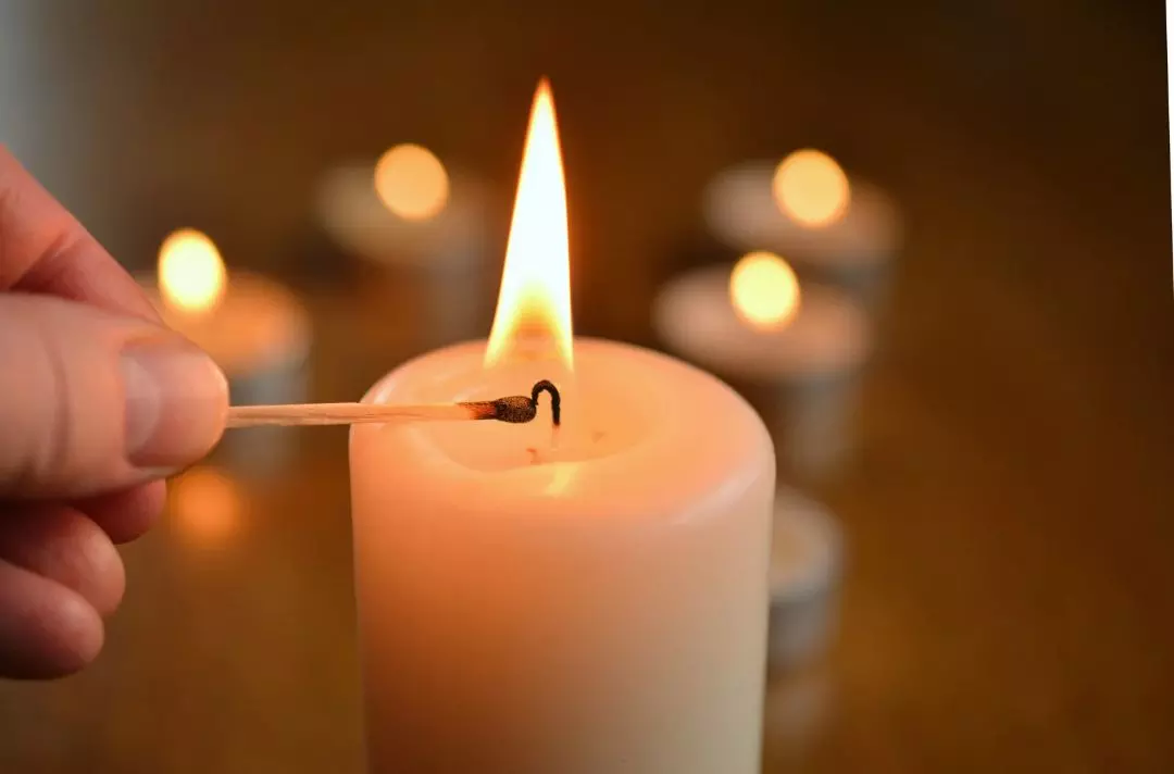 A photo of someone lighting a pillar candle in a dark room