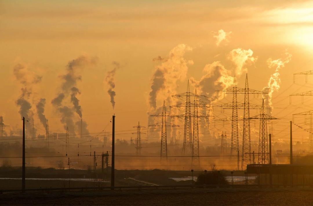A photo showing pollution rising from chimneys in an industrial scene. The sun is rising.