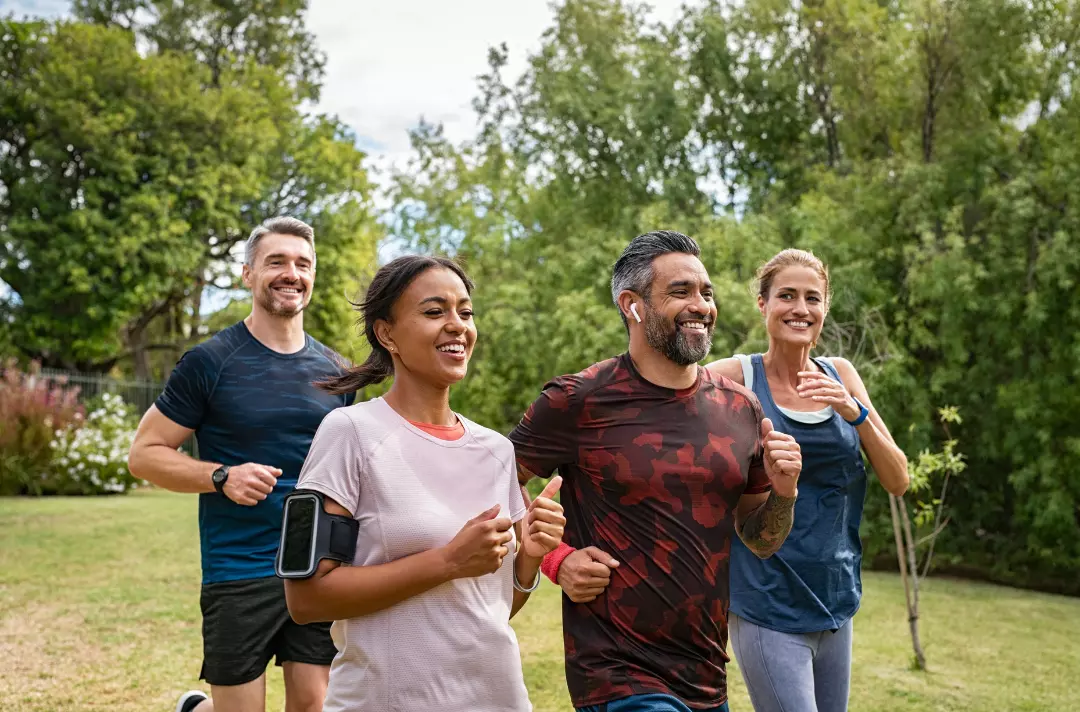 Photo shows two couples running. A couple in matching blue shirts smiles at a couple in shades of red overtakes them.