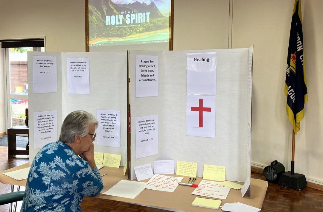 Someone sitting at a table with a prayer display featuring a cross and printed Bible verses