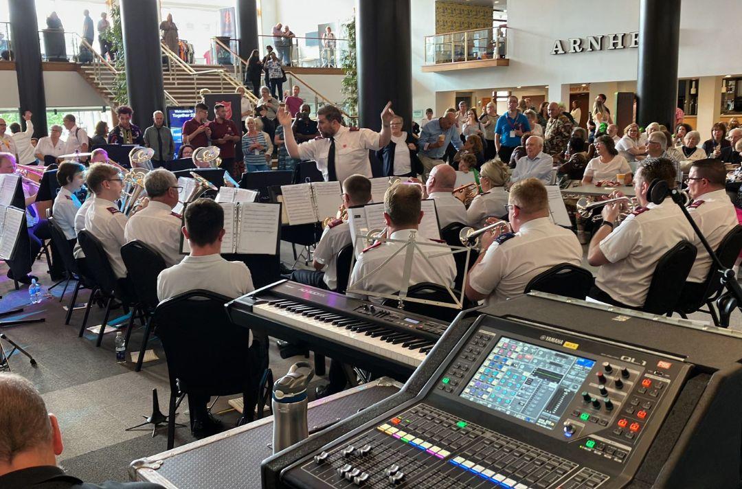 A photo of a brass band performing in the foyer of Fairfield Halls. There is a large crowd listening