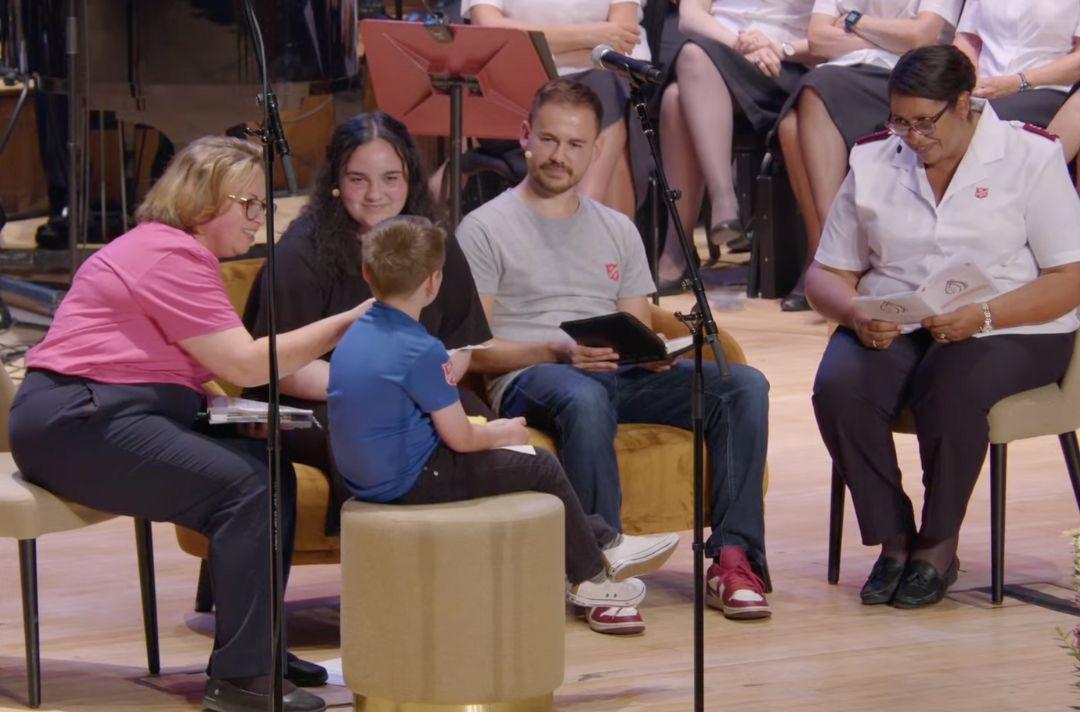A photo of four diverse people having a conversation on stage – a child, teenager, and three adults