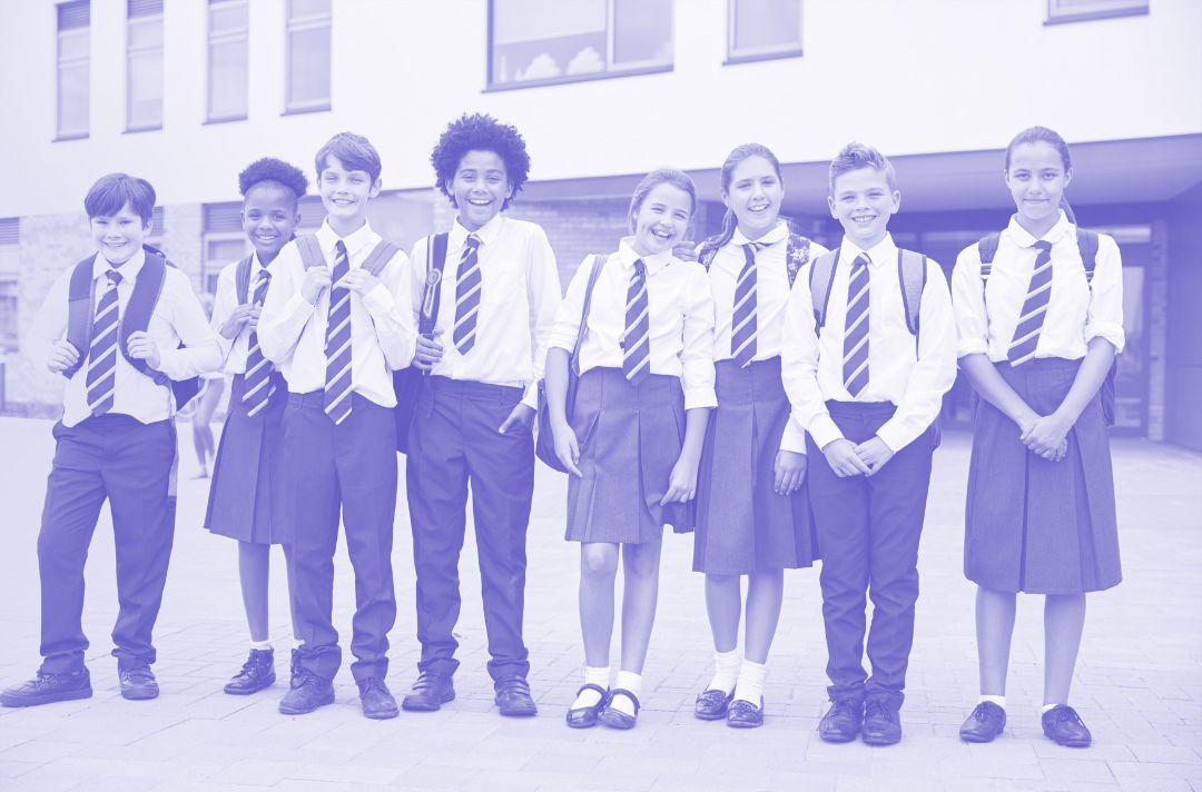 A photo of secondary school students wearing school uniform and standing outside in front of their school