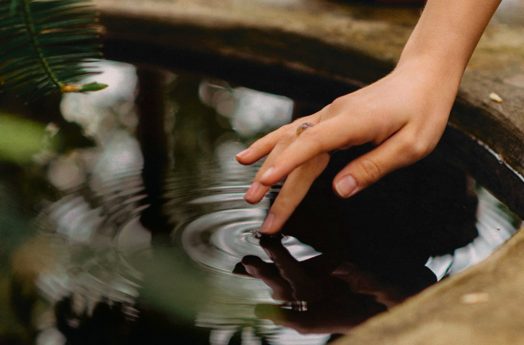 Photo shows ripples spreading out as someone lightly touches a pool of water with their middle finger.