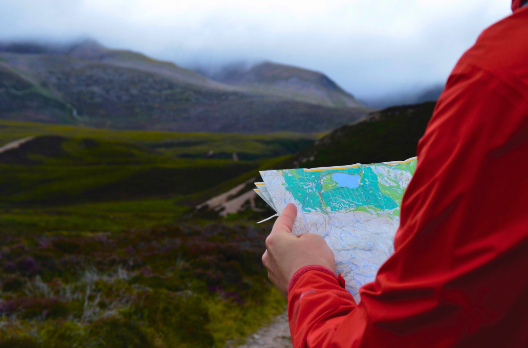 Photo shows someone holding a map as they prepare to set out across verdant, misty hills.