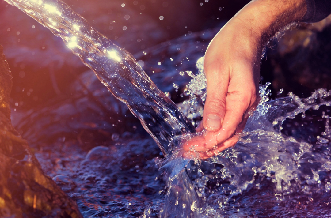 Photo shows a hand catching a natural stream of water.