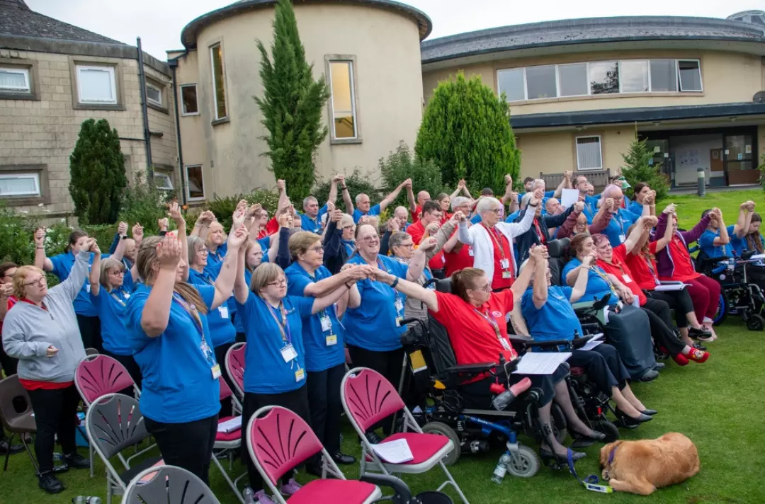 A photo shows the whole school outside, singing with their arms in the air.