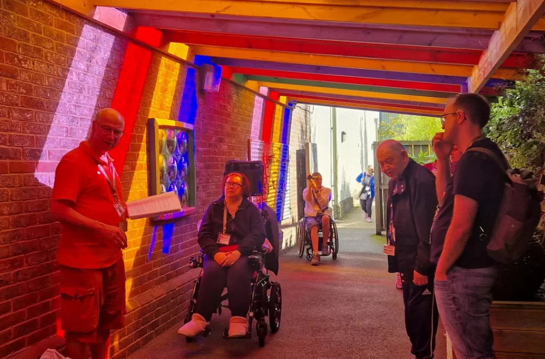 A photo shows people moving through a dimly lit tunnel-like area that is ablaze with streaks of white, red, yellow and blue light.