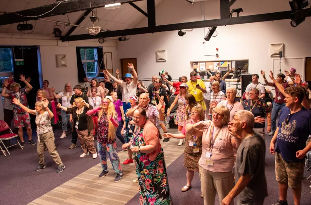 shows a Karaoke night; the lights are low and a dispersed group of people sing and wave their arms in the air.