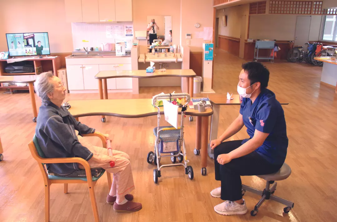A photo shows a spacious room. Two people sit at a distance. One appears to be copying the other's movements.
