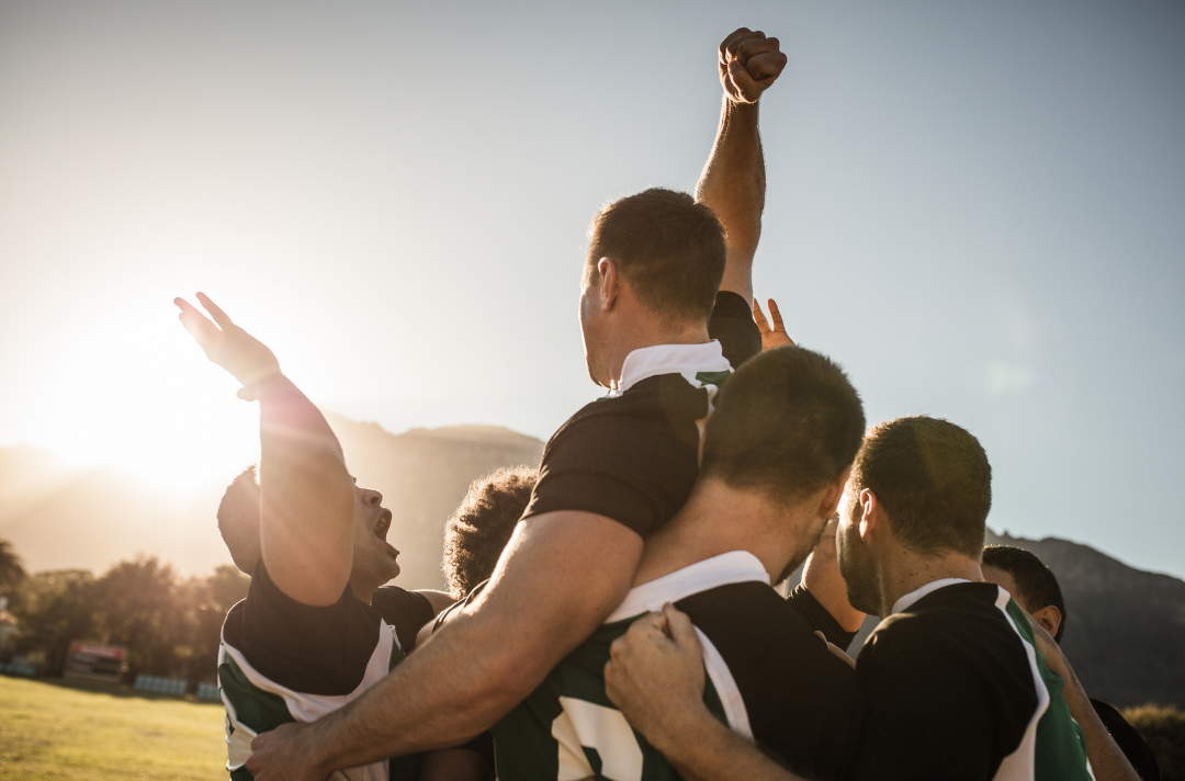 A photo shows a rugby team holding a member aloft and cheering.