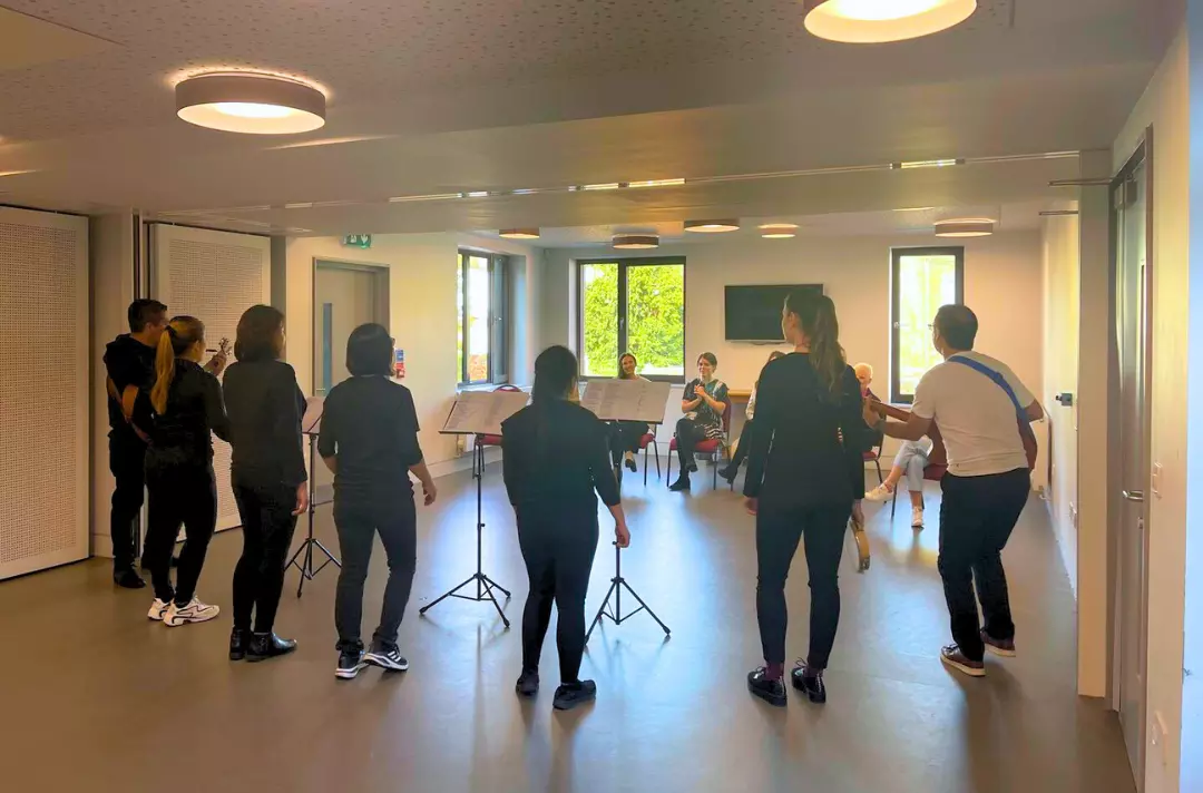 A photo shows a group of people standing in a semi-circle with their backs to the camera singing to a small group of onlookers.