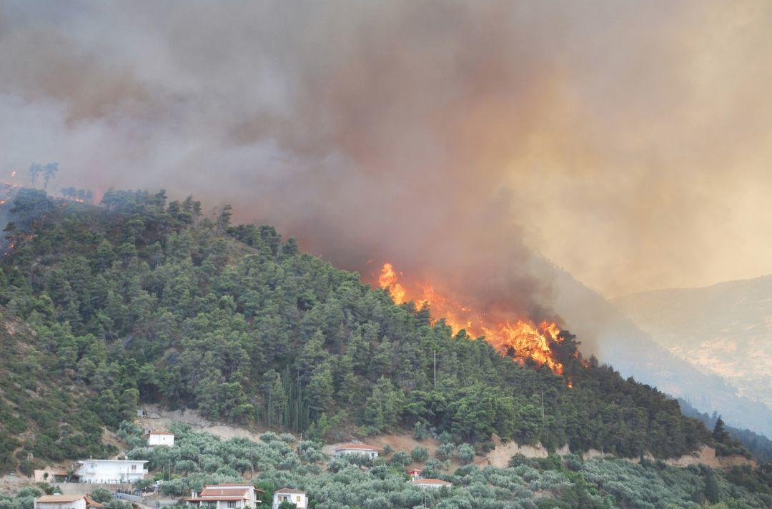 A photo of a hillside forest fire. There are Greek villas near the flames.