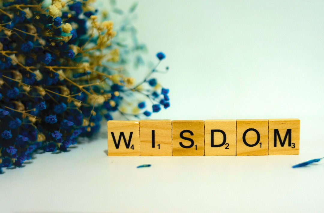 A photo shows Scrabble tiles spelling out the word "wisdom" next to a blue posy.