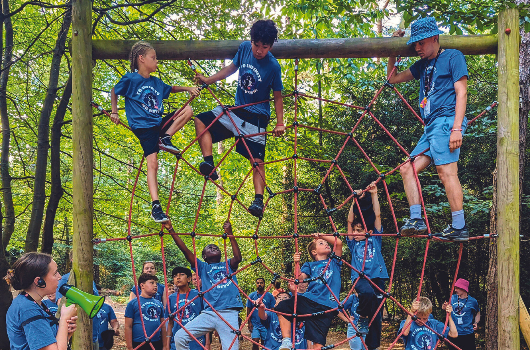 A photo shows students of the London and South East Kids Camp climbing through a spiderweb obstacle.