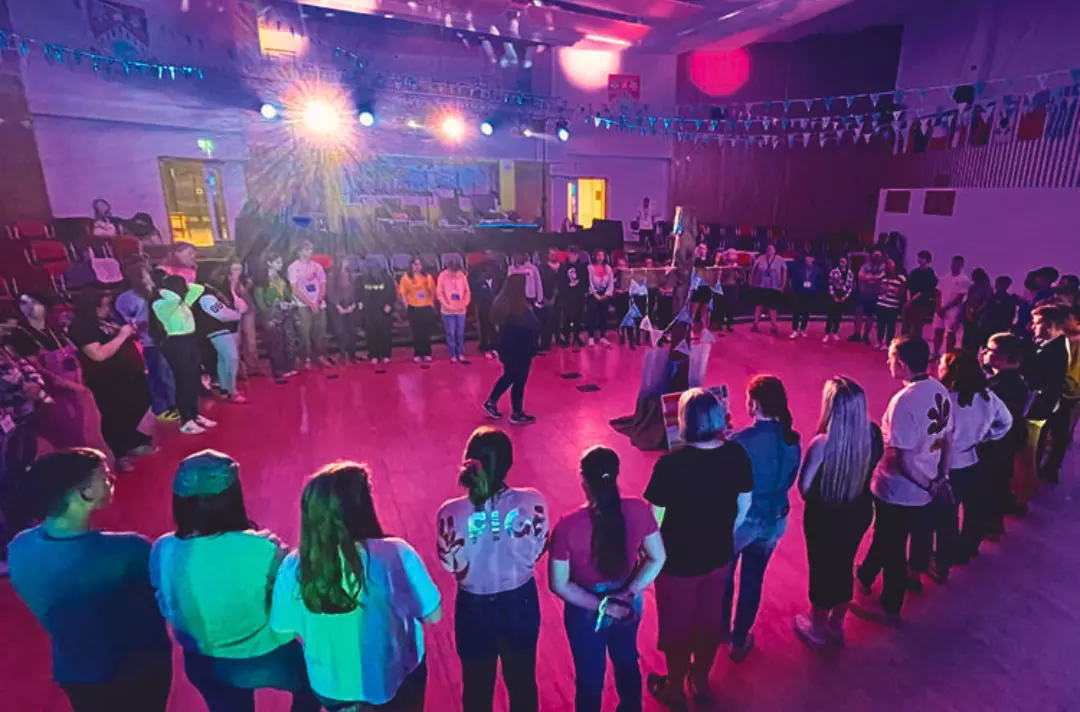 A photo shows members of the Yorkshire School of Christian Arts standing in a circle in a excitingly-lit hall.
