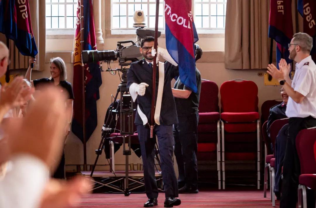 A photo shows a cadet marching in with a flag.