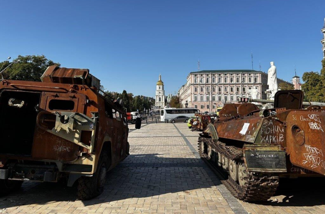 A photo shows two rusty military vehicles from behind with regular traffic up ahead.