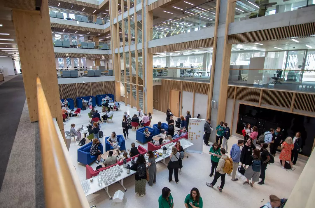 A photo of a modern office building atrium with people socialising in comfy chairs and helping themselves to tea and coffee