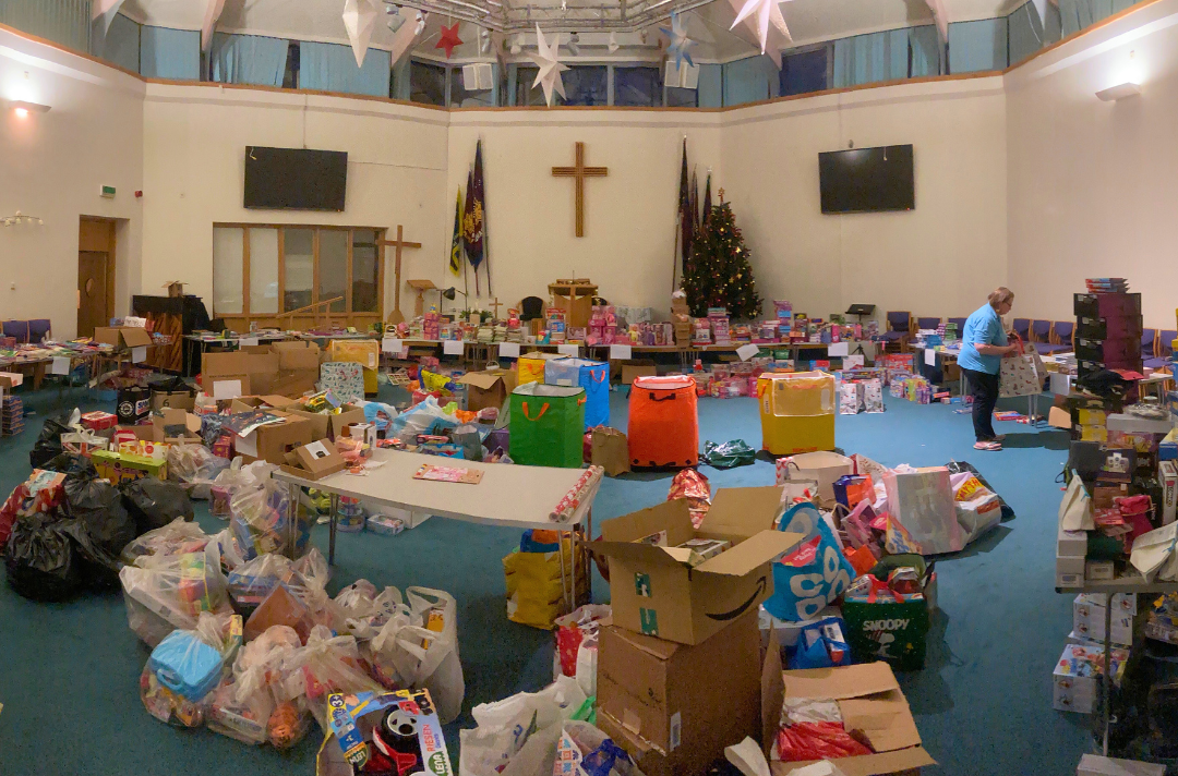 A photo shows the inside of Luton Corps, which is filled with boxes and bags of gifts for packing.