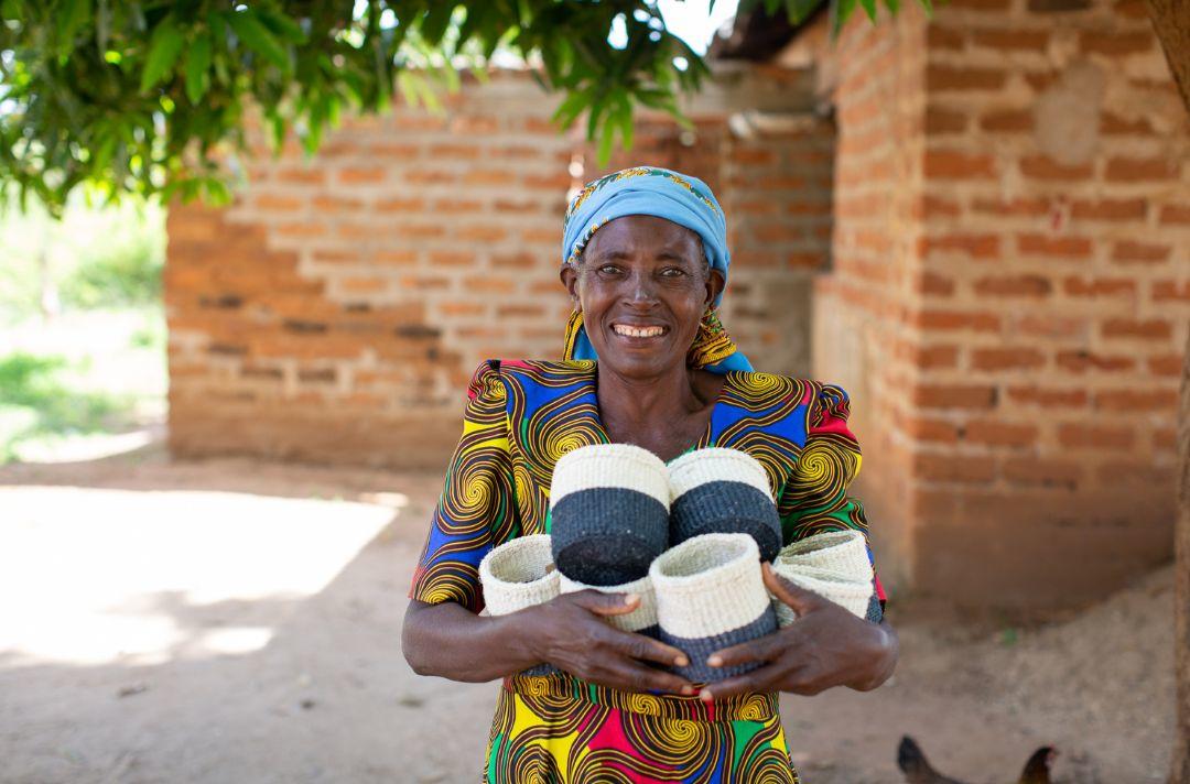 A photo of a woman from Kenya smiling and holding handmade baskets