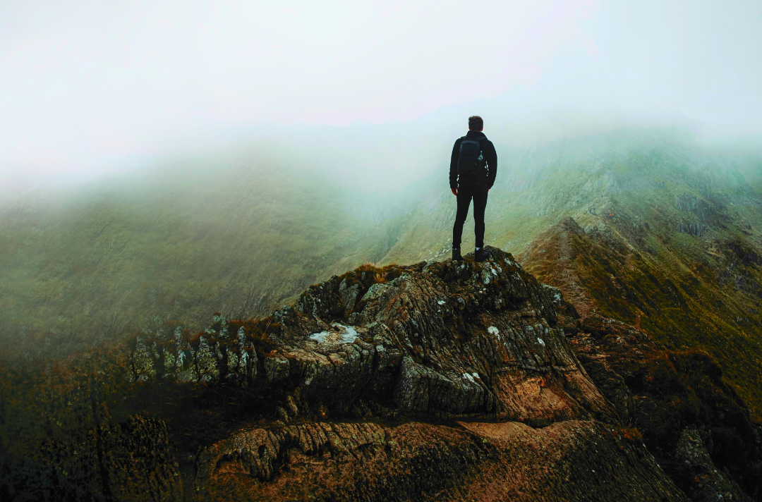 A photo shows someone standing on a rocky outcrop in front of a misty mountain.