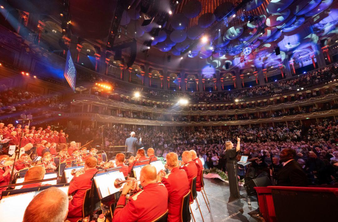 A photo of the Royal Albert Hall stage and auditorium - the International Staff Band is playing, the audience is standing to sing a carol and a BSL interpreter is signing