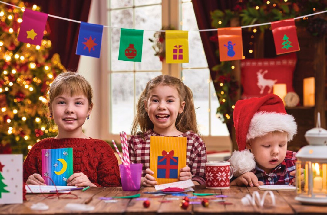 A photo shows three children holding up Christmas cards that they have decorated.