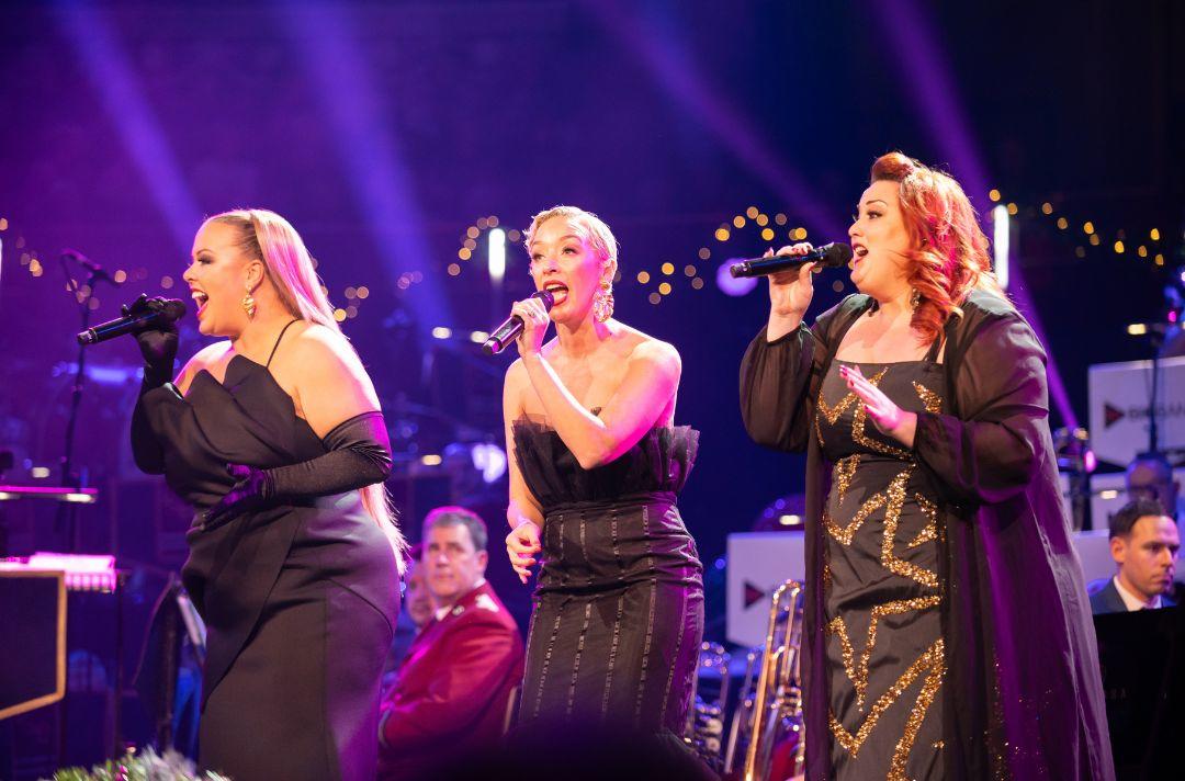 A photo of the IDolls trio singing on stage at the Royal Albert Hall wearing glamorous outfits