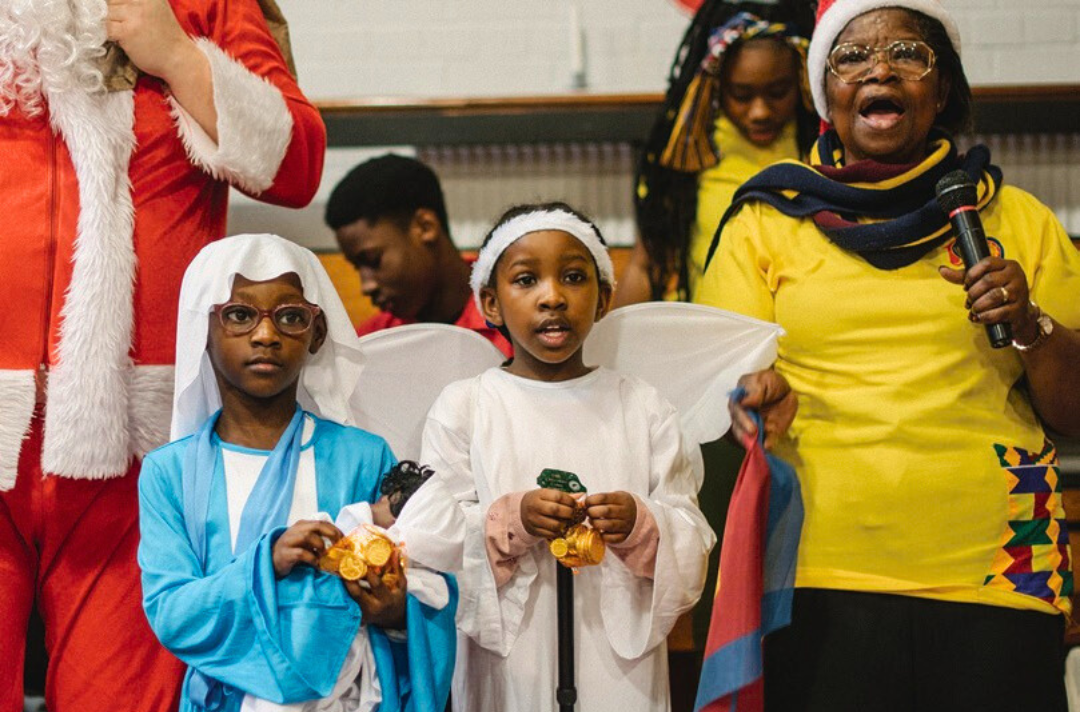A photo shows two children dressed as Nativity scene characters and an adult singing alongside them.