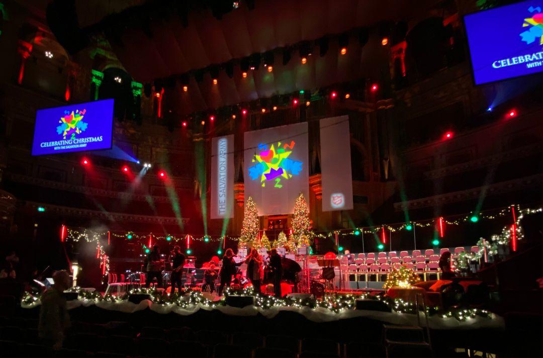 A photo of the stage of the Royal Albert Hall - you can see Christmas trees on the stage and people rehearsing 
