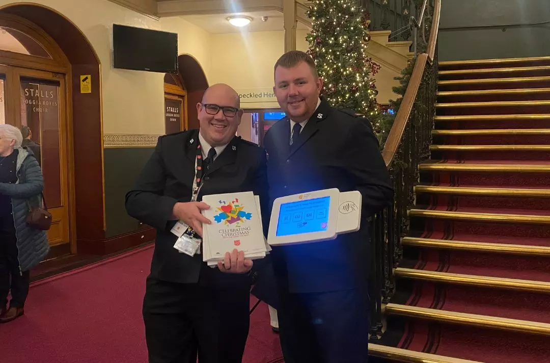 A photo of cadets Jonathan and Luke holding programmes and a card reader for donation