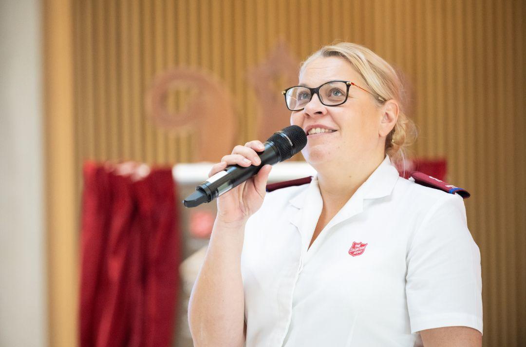 A photo of Steph Lamplough performing her poem at the opening ceremony - she's wearing Salvation Army uniform and speaking into a microphone