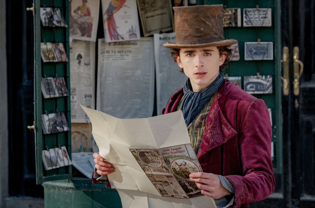 A scene from the movie Wonka shows Timothée Chalamet as Wonka looking up from a newspaper. Jaap Buittendijk © 2023 Warner Bros. Entertainment Inc. All Rights Reserved.
