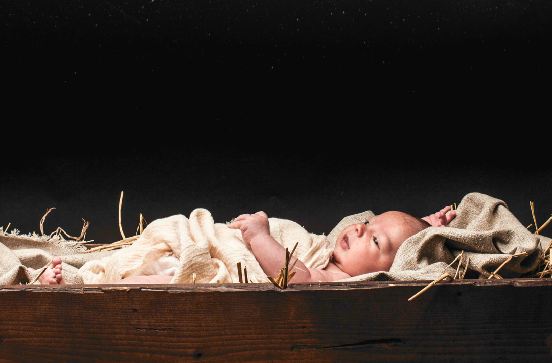 A photo shows the baby Jesus lying in a manger in front of a black backdrop.
