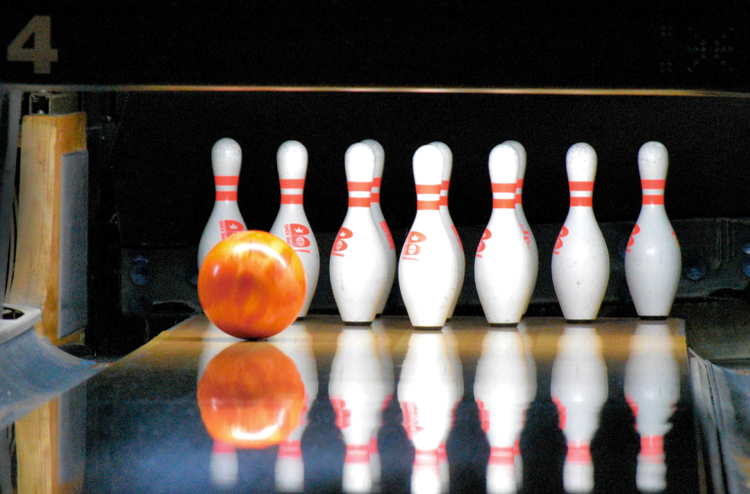 A photo shows a bowling ball about to hit skittles in a bowling alley.