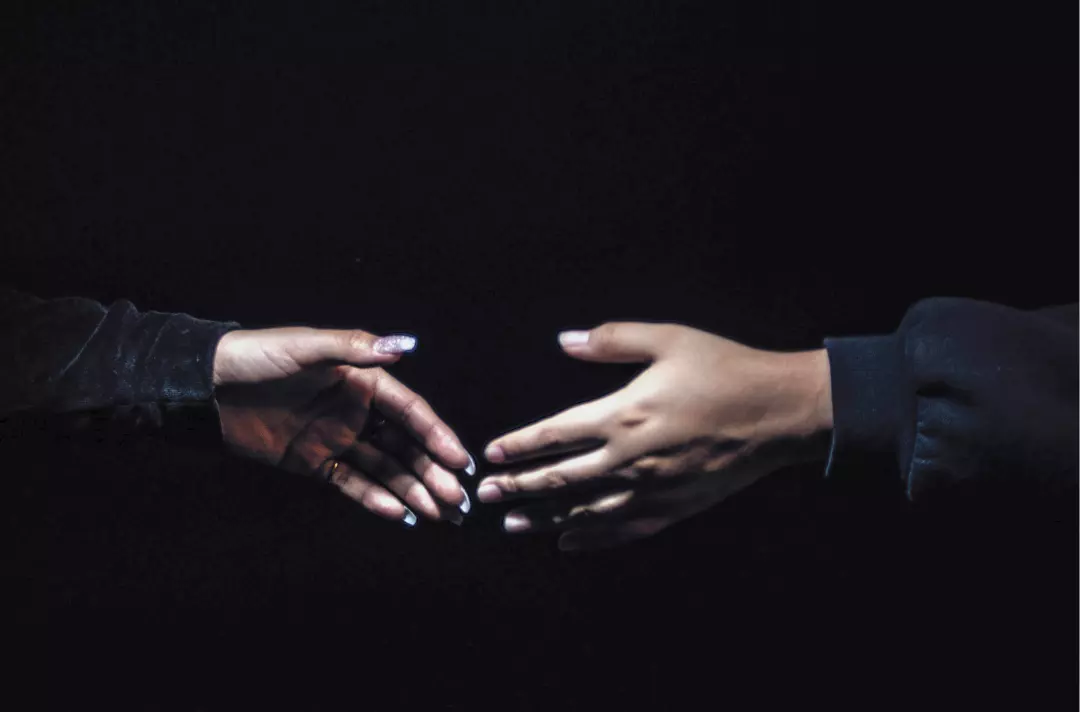 A photo shows two hands reaching for each other in the dark.