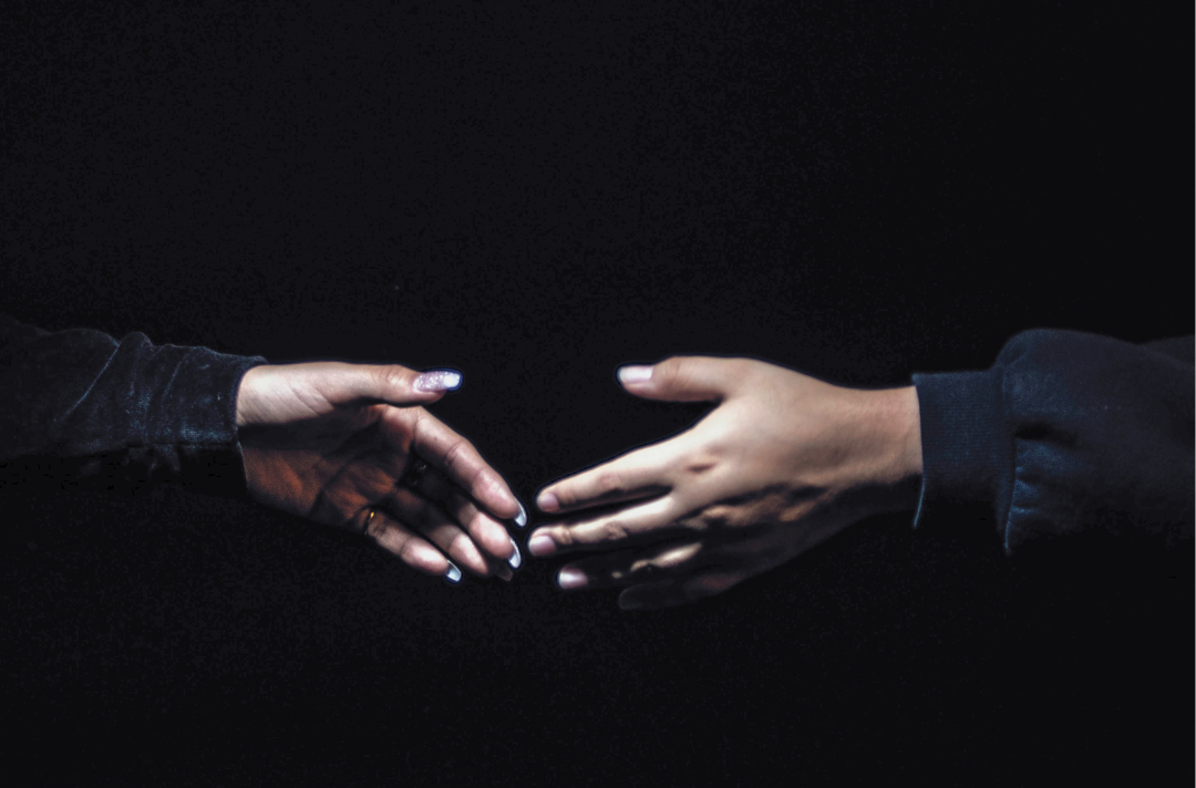 A photo shows two hands reaching for each other in the dark.