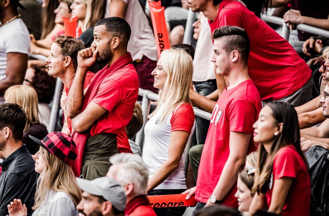A photo of a diverse group of people all wearing red watching their sports team