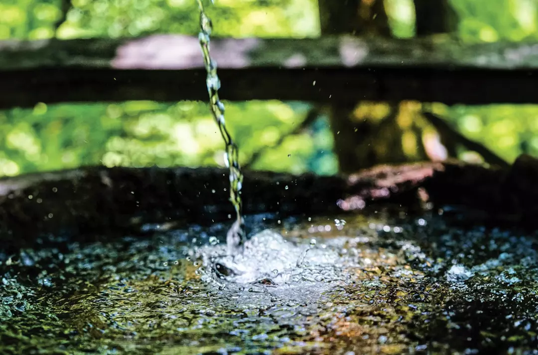 A photo shows water being poured into a well.