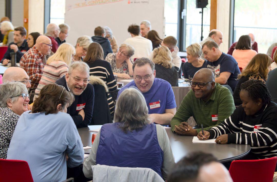 A photo of people smiling and having conversations round tables