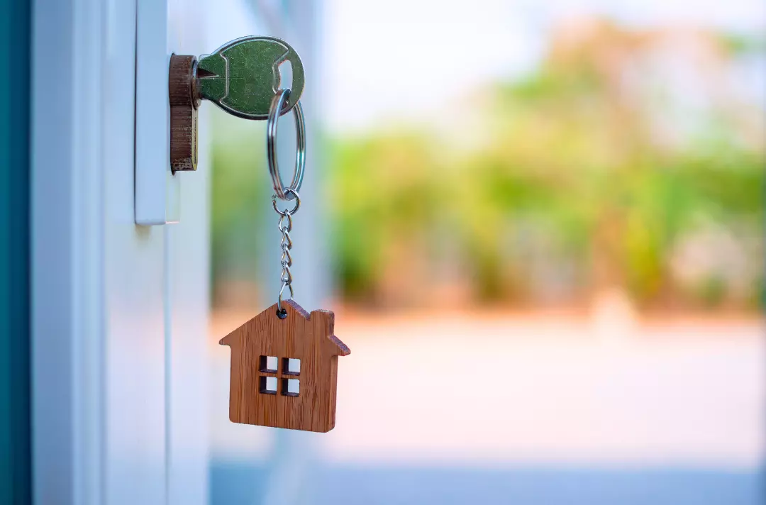A photo shows a key the lock of a front door. From the key hangs a house-shaped keyring.