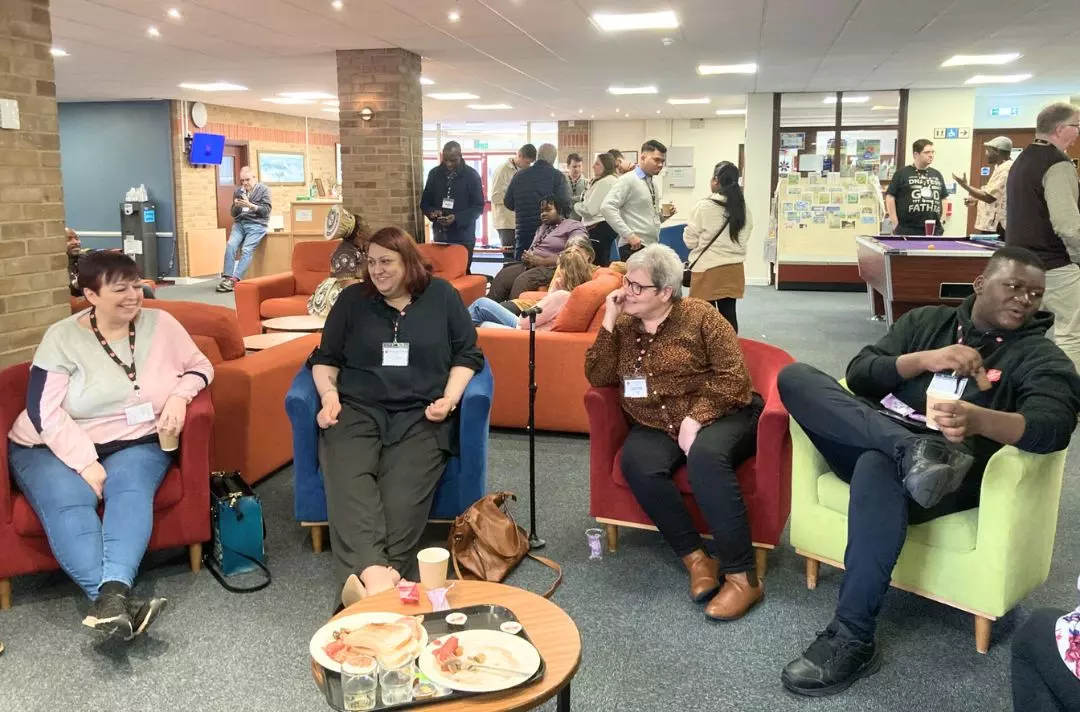 A photo shows a group of people from different backgrounds smiling and laughing while sat in comfy chairs.