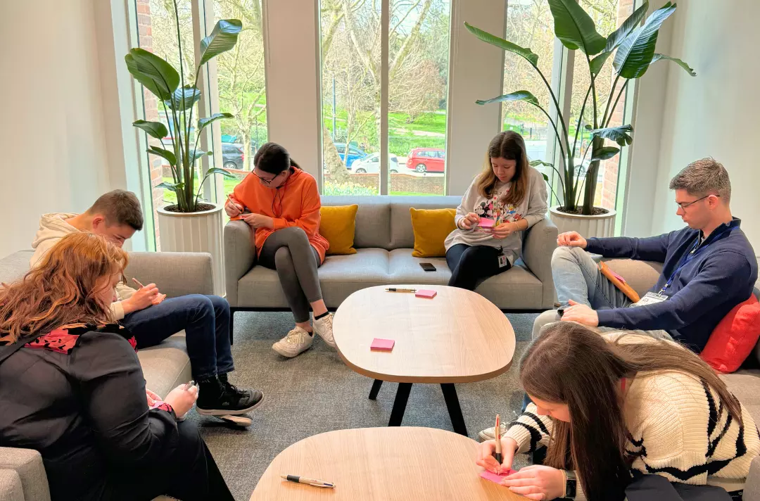 A photo shows members of the Territorial Justice and Reconciliation Youth Forum in discussion while sat around tables in a small meeting room in THQ.