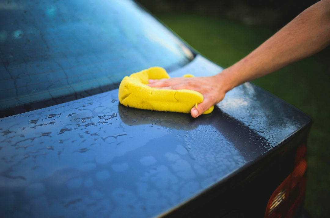 A photo shows someone washing a car with a bright yellow sponge.