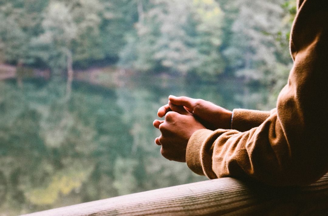 A photo shows someone praying by a lake, with particular focus given to the hands.