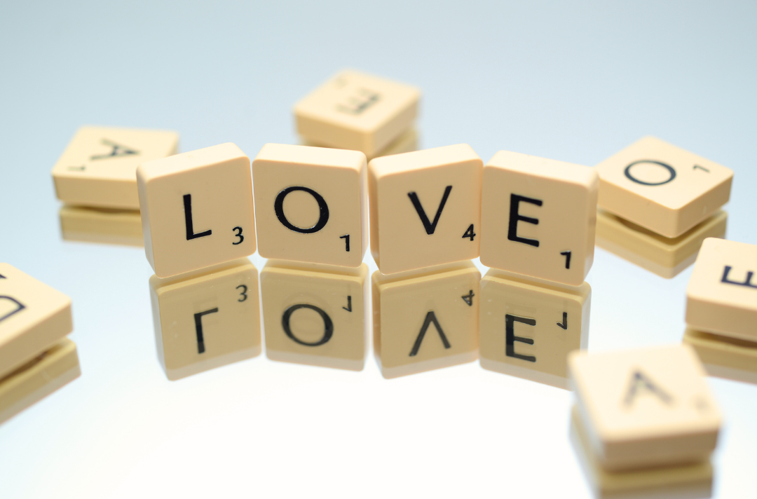 A photo shows Scrabble tiles spelling out the word "love" on a mirrored surface.