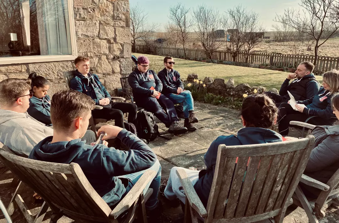 A photo shows a group of people taking part in the Terrain programme sat outside on garden chairs in a circle.
